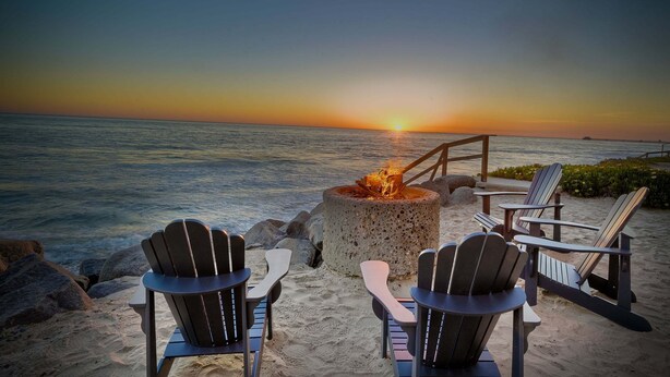 A beach setting with a fire pit, Adirondack chairs, and a view of the sunset over the ocean. - 1409 S Pacific Street (Oceanside)