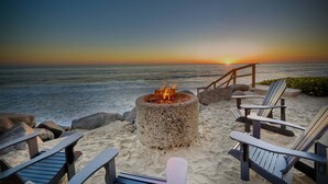 A beach setting with a fire pit, Adirondack chairs, and a view of the ocean at sunset. - 1409 S Pacific Street (Oceanside)