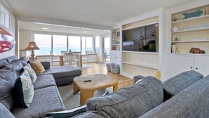 Ein geräumiges Wohnzimmer mit großem Fenster, einem Essbereich und einem Bücherregal mit einem Schild mit der Aufschrift 'Beach'.