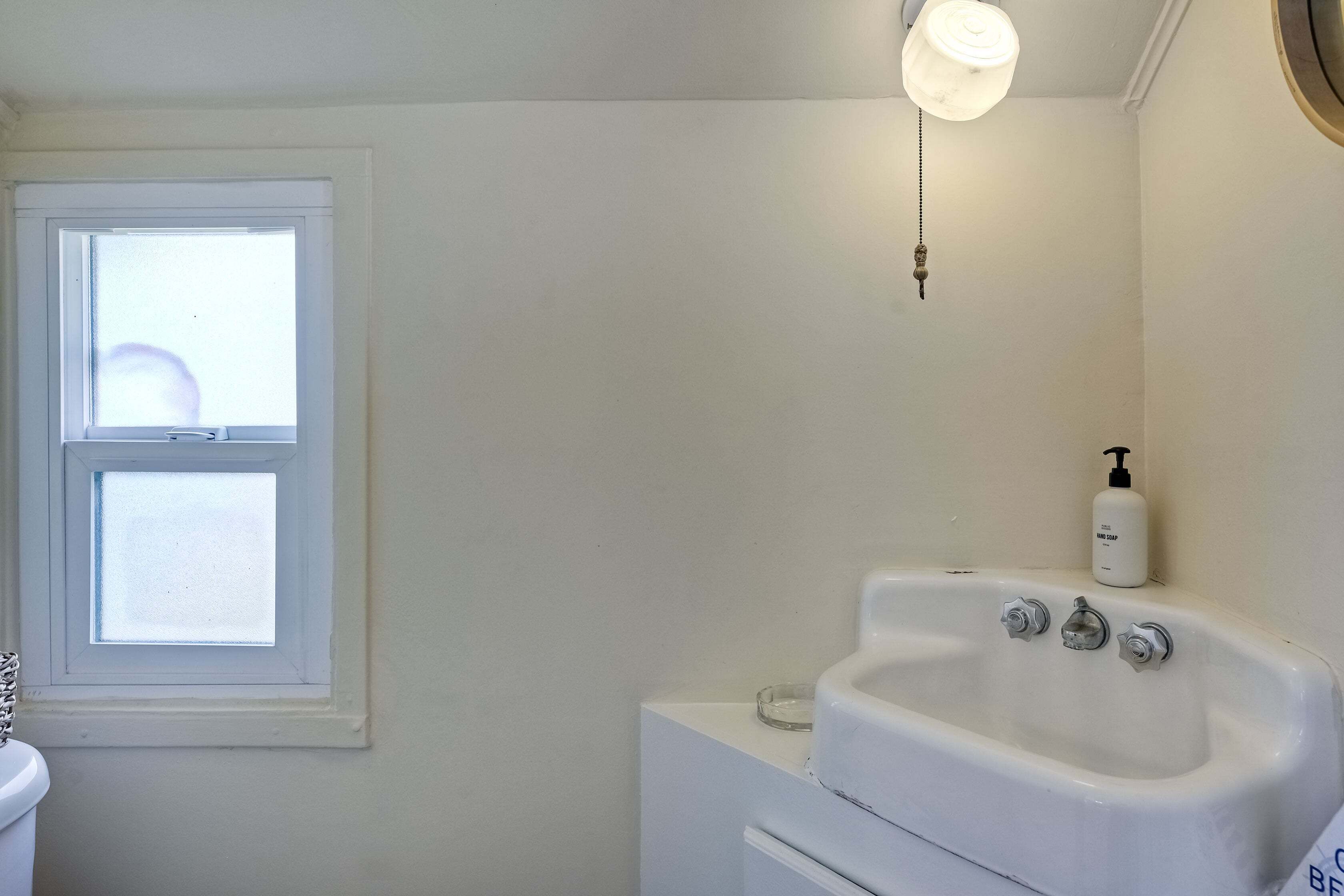 A bathroom with a window, a sink, and a bottle of hand soap.