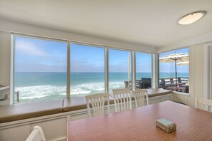 A dining area with a view of the ocean, large windows, and a wooden table. - 1745 S Pacific (Oceanside)