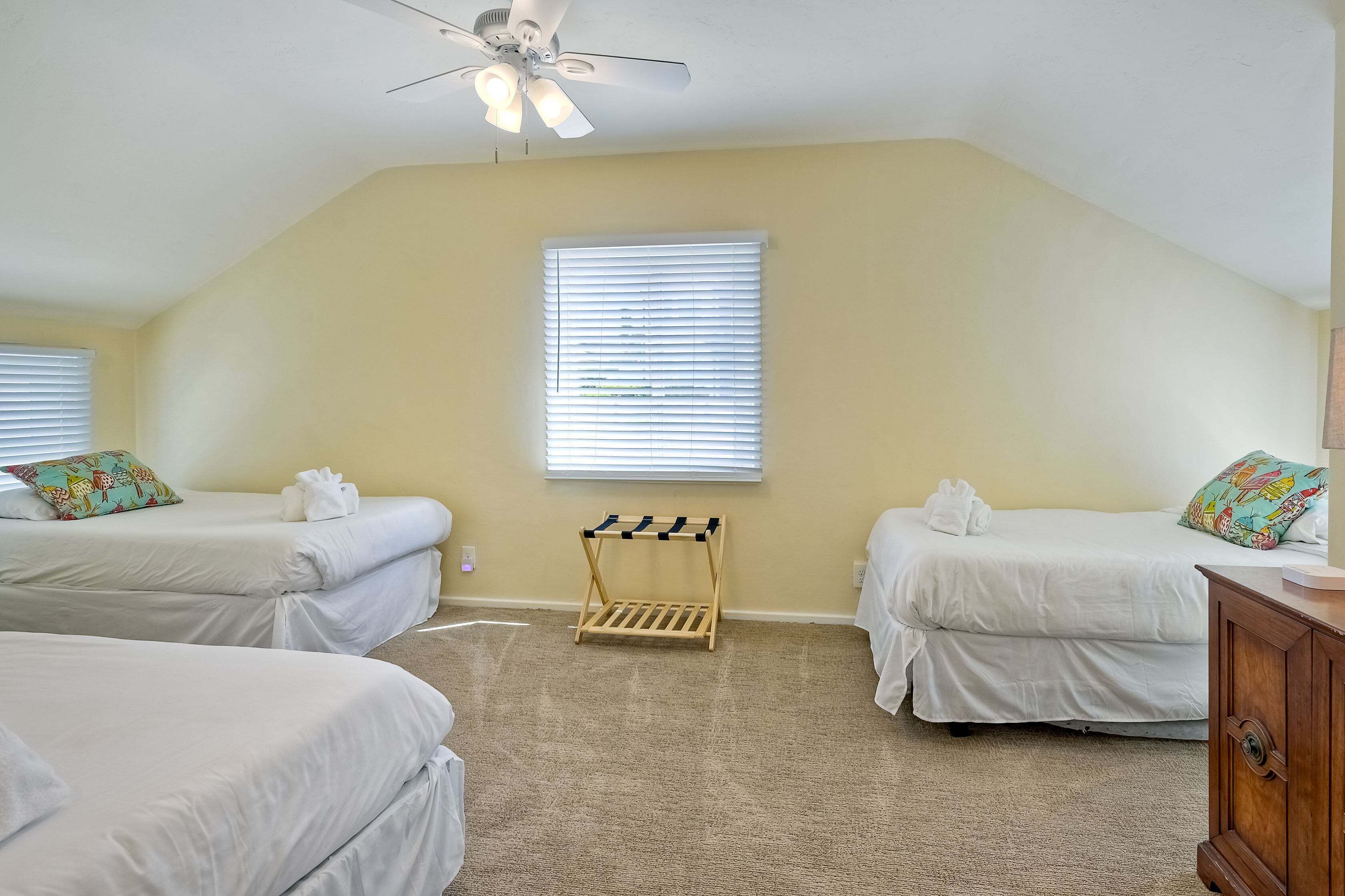 A hotel room with two beds, a ceiling fan, a wooden rack, and a window with blinds.