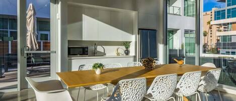 Una cocina moderna con una mesa de comedor de madera y sillas blancas, ventanas amplias y vistas a la ciudad.