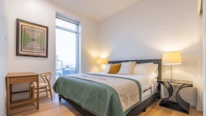 Een keurig opgeruimde slaapkamer met een bed, bedlampjes, een bureau en een stoel.
