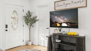 A living room with a television mounted on the wall, a potted plant, and a framed sign above the TV.
