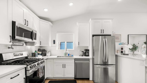 A modern kitchen with white cabinets, stainless steel appliances, and a black rug.