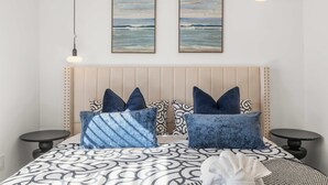 A bedroom with a bed, two wall-mounted paintings, a headboard, and two bedside tables.