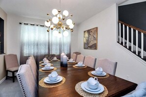 Comedor con una mesa de madera dispuesta para seis comensales, rodeada por seis sillas, una araña y un amplio ventanal con cortinas.
