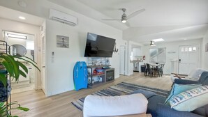 Een moderne woonkamer met een flatscreen televisie, een blauwe koelkast, een houten stoel en een blauwe bank met opvallende kussens.