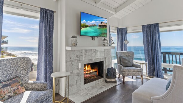 A living room with a fireplace, a television, and a view of the ocean. - 1317 S Pacific - Entire Home (Oceanside)