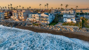 A coastal residential area with multi-story houses, a rocky shoreline, and palm trees. - 1317 S Pacific - Entire Home (Oceanside)