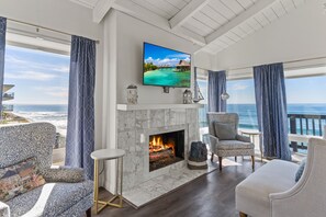 A living room with a fireplace, a television, and a view of the ocean. - 1317 S Pacific - Entire Home (Oceanside)