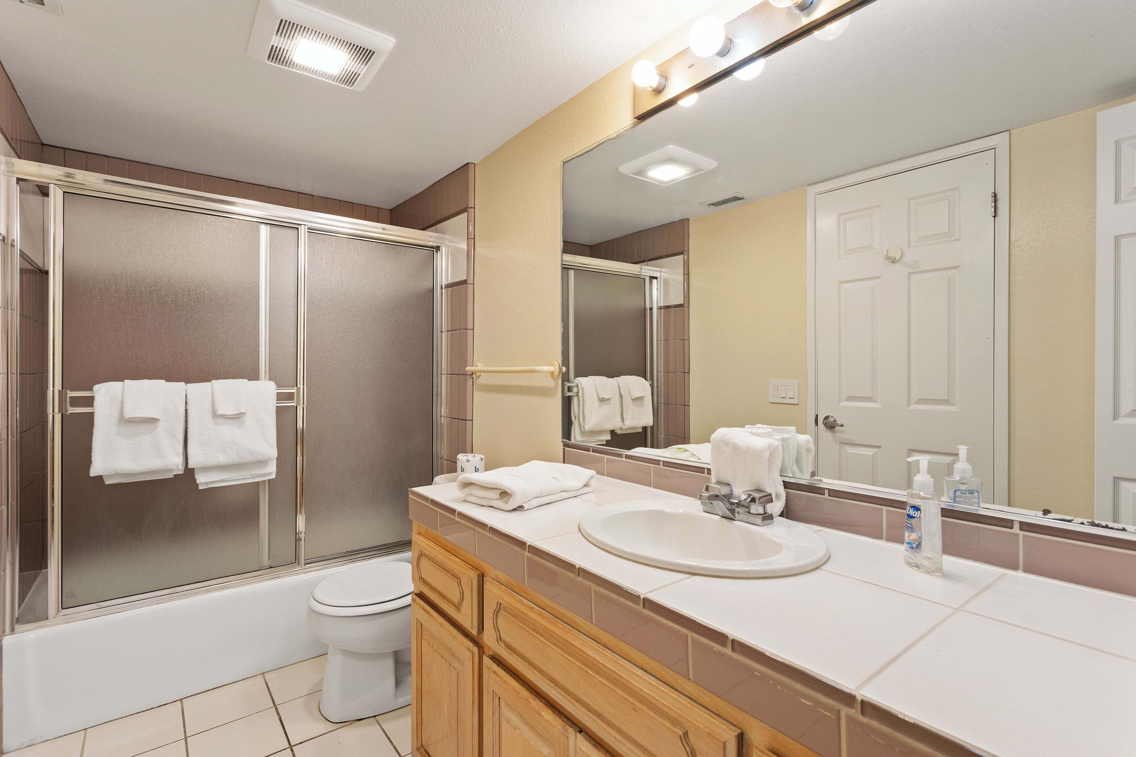 A bathroom with a shower, toilet, sink, and mirror.