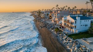 A beachfront property with a rocky shoreline, multiple-story buildings, and a pier extending into the ocean. - 1317 S Pacific - Entire Home (Oceanside)