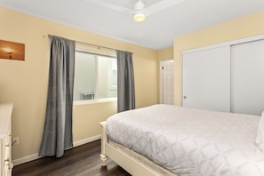Un dormitorio con cama, ventana con cortinas, puerta y ventilador de techo.