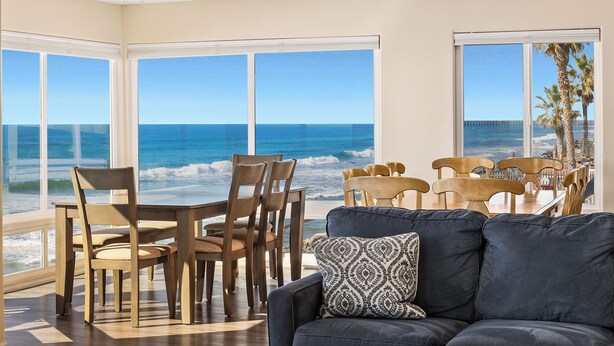 A room with large windows overlooking the ocean, wooden furniture, and a dark-colored sofa. - 1317 S Pacific - Unit C (Oceanside)
