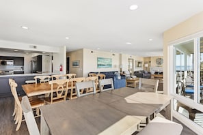 Amplia sala de estar con mesa de comedor, sillas de madera, sofá y vistas a través de grandes ventanales.