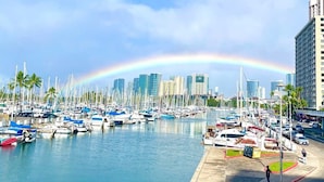 A marina with numerous boats docked, a city skyline in the background, and a rainbow in the sky. - @ Marbella Lane - Cozy 2BR w/ Amazing Ocean Views (Honolulu)