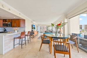 A modern kitchen with wooden cabinets, a central island, and a dining area with a glass table and wooden chairs. - @ Marbella Lane - Cozy 2BR w/ Amazing Ocean Views (Honolulu)