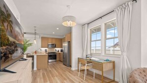 Une cuisine moderne avec des meubles en bois, un réfrigérateur en acier inoxydable et un coin repas comprenant une table et des chaises en verre.