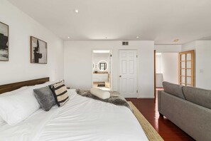 A bedroom with a large bed, a grey sofa, and a door leading to a bathroom. - @ Marbella Lane - Vibrant 5BR Home in Daly City (Daly City)