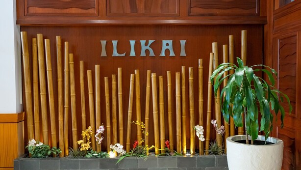A reception area with a wooden backdrop, bamboo sticks, and a potted plant. - @ Marbella Lane Dreamy Sunset Views by the Sea (Honolulu)
