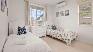 A bedroom with two beds, a window with curtains, and a wall-mounted air conditioner. - @ML Ocean View, Golf, Gazebo and Bbq, we Have All! (Waianae)