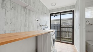 Une buanderie avec un plan de travail en bois, un lave-linge et une porte-fenêtre coulissante donnant sur un balcon.