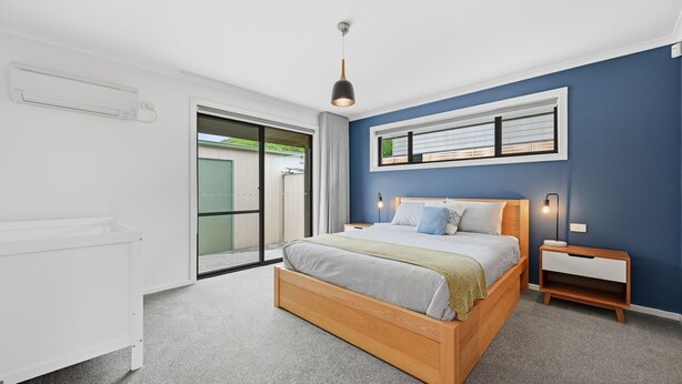Une chambre moderne avec un lit en bois, une table de chevet, une lampe de chevet et une vue sur l’extérieur, accessible par une porte coulissante.