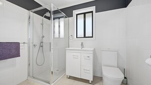 Ein modernes Badezimmer mit Duschkabine aus Glas, einem weißen Waschbecken mit Spiegel darüber und einer Toilette.