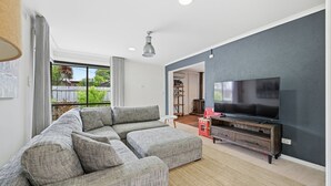 Un salon moderne avec un canapé d’angle, un téléviseur à écran plat et un meuble de rangement en bois.