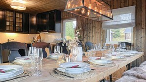 Interior de madera con una larga mesa de comedor dispuesta para una comida, con vasos y platos transparentes.