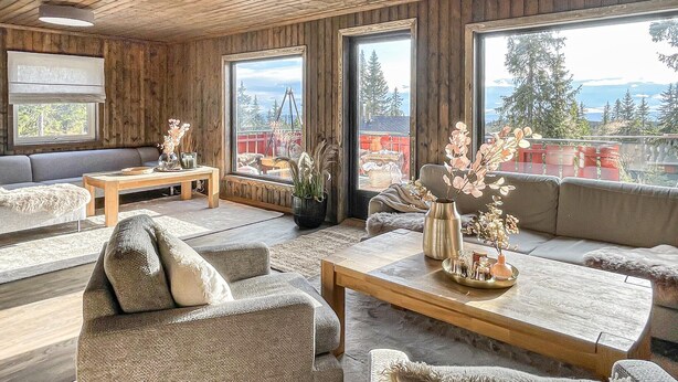 Una sala de estar acogedora con techo de madera, ventanas amplias y vistas a árboles y montañas.