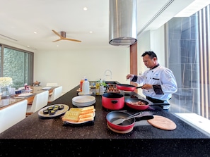 A modern kitchen with a chef preparing food, a dining area with a stone wall, and a large window. - Sea Theatre Kata (Karon)