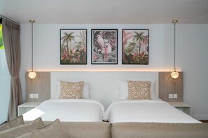 Una cama doble con ropa de cama blanca y almohadas estampadas, un cabecero con una lámpara de diseño geométrico, y tres cuadros con motivos tropicales sobre la cama.