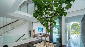 Un intérieur moderne avec un escalier, un coin salon offrant une vue agréable et un bac à plantes contenant un arbre.