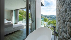 A modern bedroom with a large bed, a glass door leading to a balcony, and a view of the surrounding landscape. - Sea Theatre Kata (Karon)