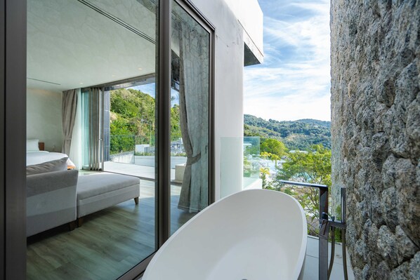 Une chambre moderne avec un grand lit, une porte vitrée donnant sur un balcon et une vue sur le paysage environnant.