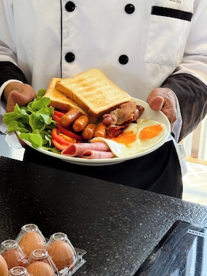 A person holding a plate of food with a sandwich, eggs, bacon, tomatoes, and sausages. - Sea Theatre Kata (Karon)