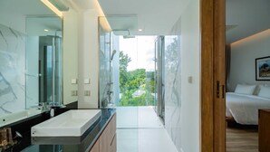 A modern bathroom with a large mirror, a glass shower enclosure, and a view of a green landscape. - Sea Theatre Kata (Karon)