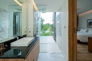 Une salle de bain moderne avec un grand miroir, une douche en verre et une vue sur un paysage verdoyant.