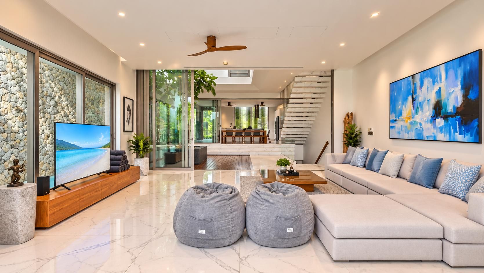 A modern living room with a large flat-screen TV, a sofa set, and two bean bags.
