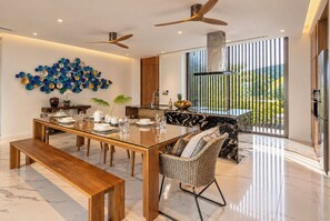 A modern kitchen with a marble countertop, a dining area with a wooden table and bench, and a ceiling fan. - Sea Theatre Kata-Villa Privé, Villa Alté, Villa Maré-Seaview, Maid, Gym, Kata (Karon)