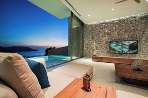 Un salon moderne avec un mur en pierre, une grande fenêtre donnant sur une piscine et un téléviseur à écran plat fixé au mur.