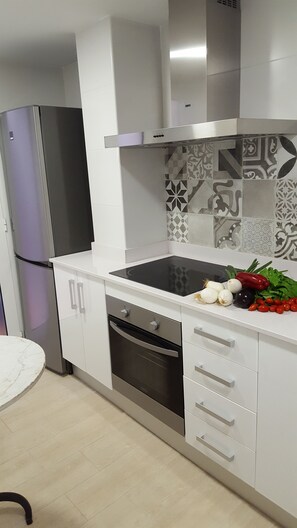 Eine moderne Küche mit weißen Schränken, einer schwarzen Induktionskochplatte, einem eingebauten Backofen und einem Edelstahl-Kühlschrank.