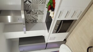 Uma cozinha moderna com armários brancos, um fogão por indução preto, forno embutido e uma geladeira de aço inoxidável.