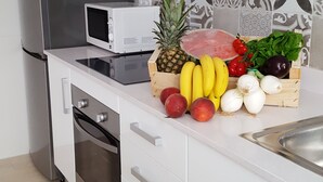 Cozinha moderna com frigorífico de aço inoxidável, micro-ondas e expositor de madeira para fruta e legumes.