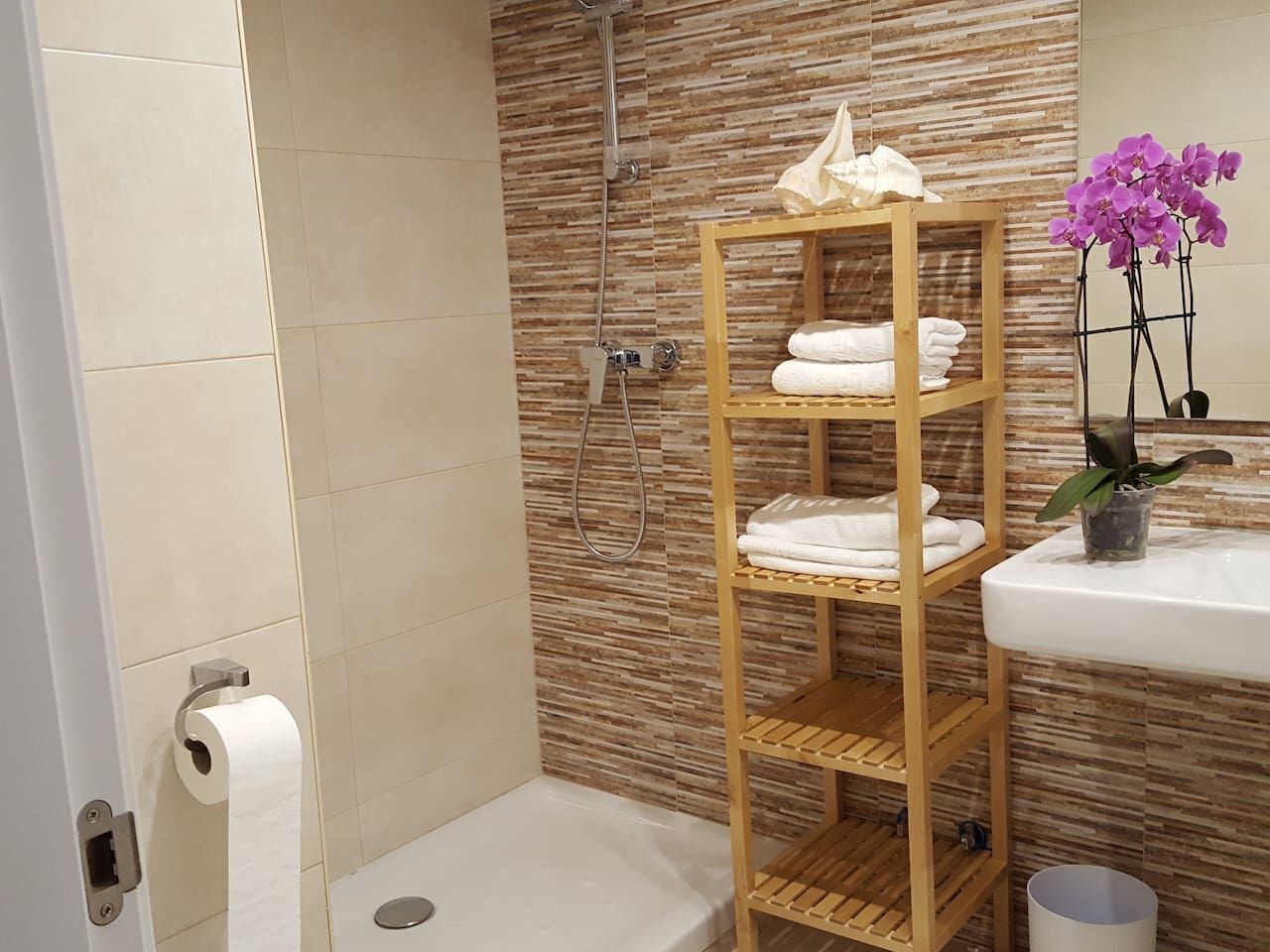 A bathroom with a shower, toilet, and a shelf with towels.
