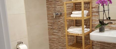 A bathroom with a shower, toilet, and a shelf with towels.