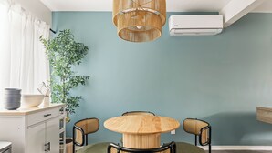A dining area with a round wooden table and four chairs, a hanging wicker lamp, a potted plant, and a white air conditioning unit on the wall. - Vibrant 2-bedroom guest house with AC in Long Beach near Retro Row (Long Beach)